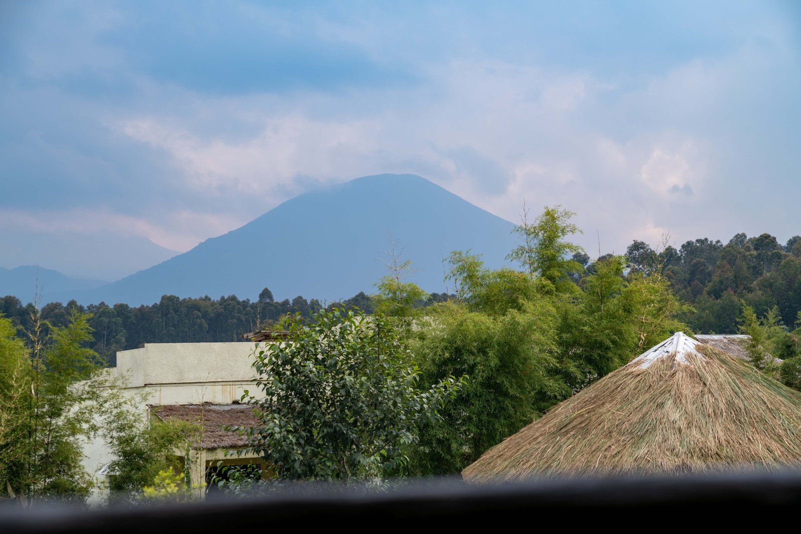 Volcano at dusk above a thatched lodge roof, Musanze